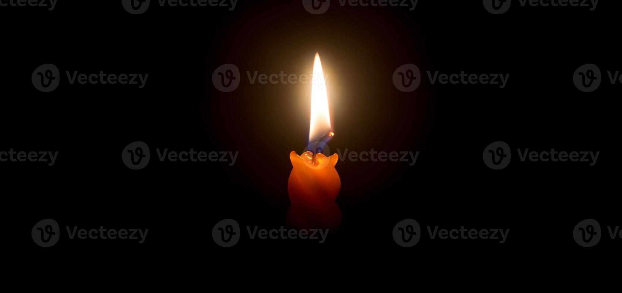 una sola llama de vela encendida o luz que brilla en una hermosa vela espiral naranja sobre fondo negro u oscuro en la mesa de la iglesia para Navidad, funeral o servicio conmemorativo con espacio para copiar foto