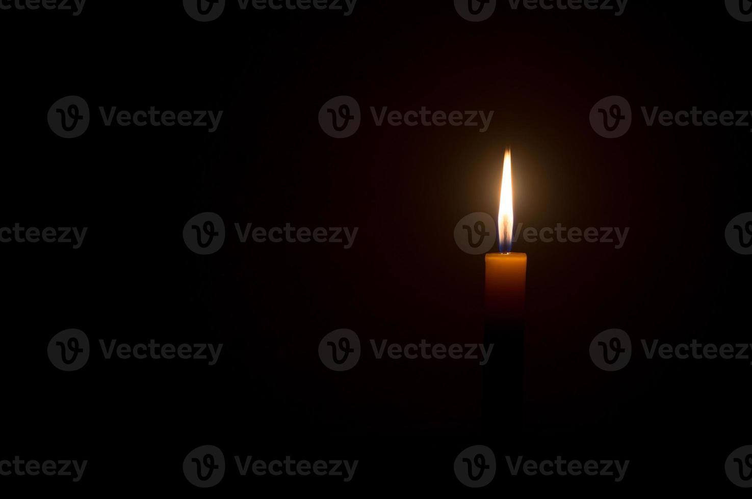 Single small yellow candle light glowing isolated on black or dark background on table in church or temple for Christmas, funeral or memorial service photo