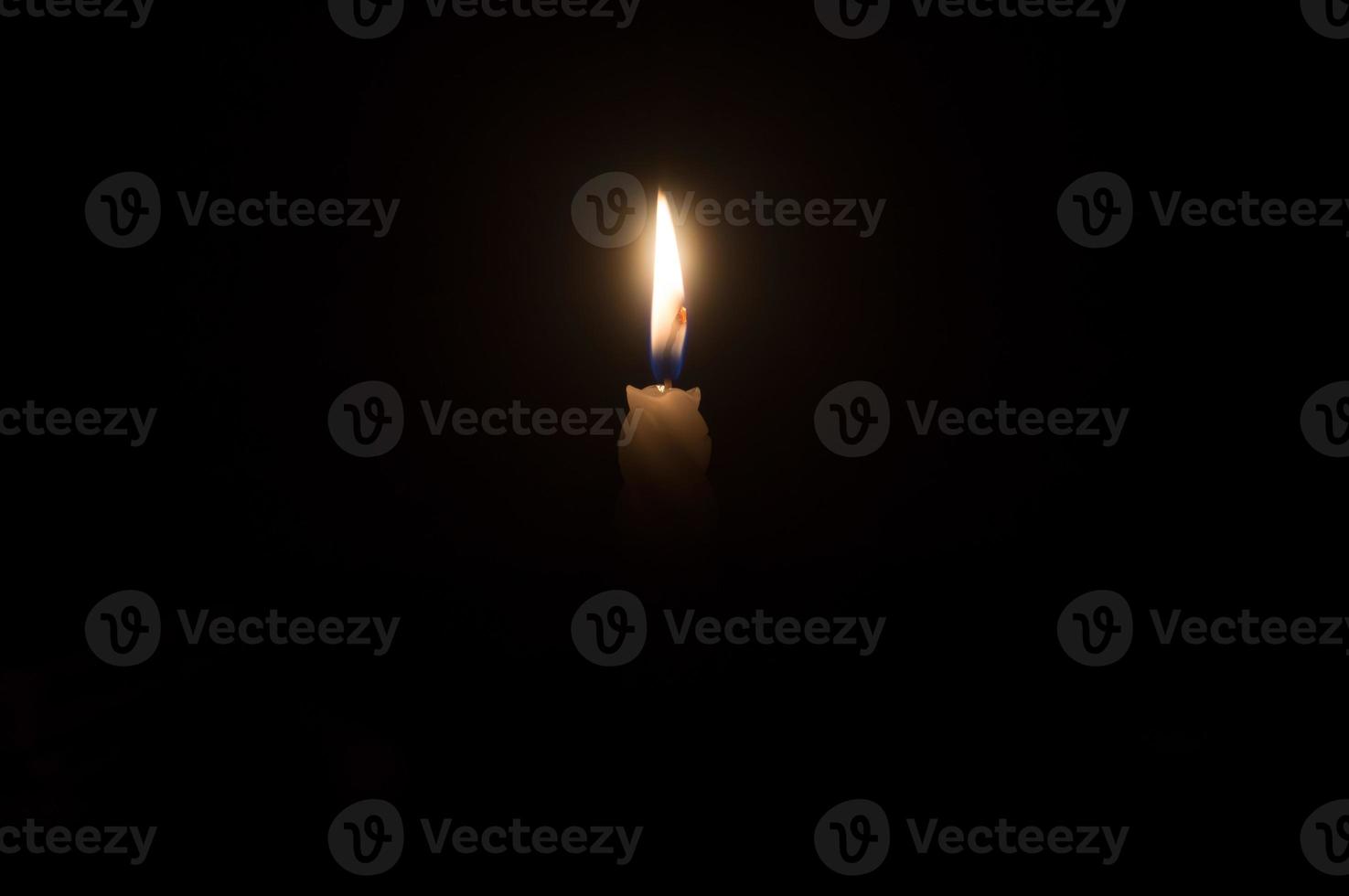 A single burning candle flame or light glowing on a beautiful spiral white candle on black or dark background on table in church for Christmas, funeral or memorial service with copy space photo
