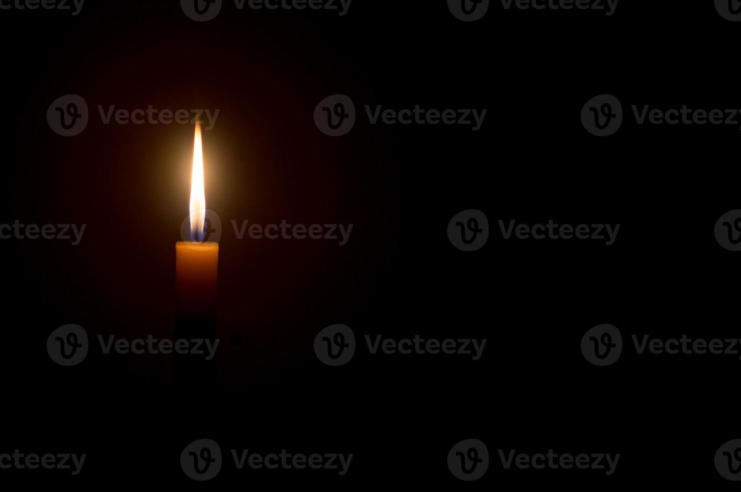 A single burning candle flame or light glowing on a Single small yellow candle light glowing is isolated on black or dark background on table in church or temple for Christmas, funeral or memorial photo