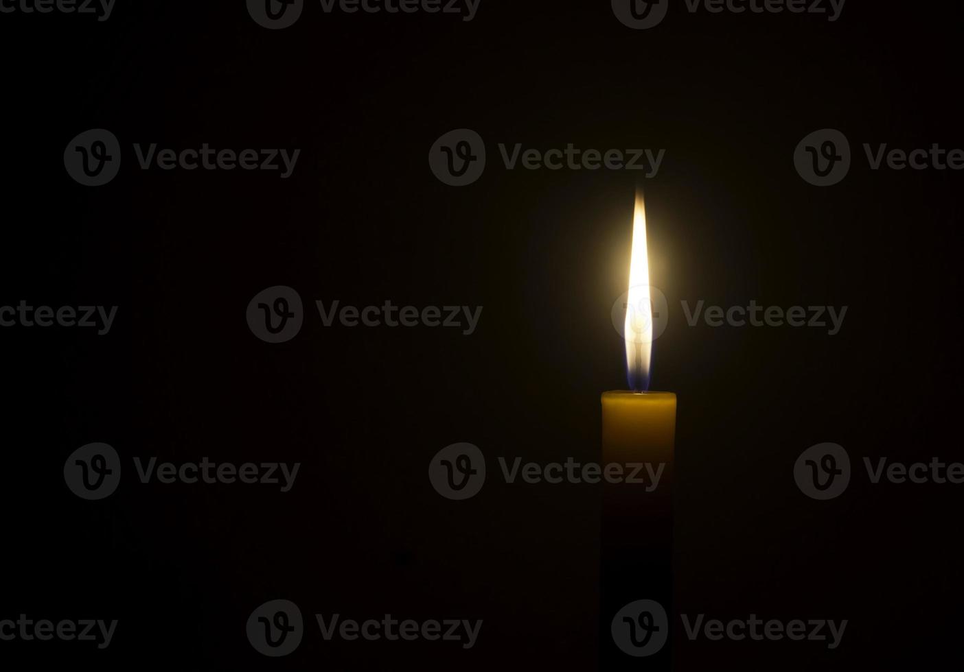 A single burning candle flame or light glowing on an orange candle on black or dark background on table in church for Christmas, funeral or memorial service with copy space photo
