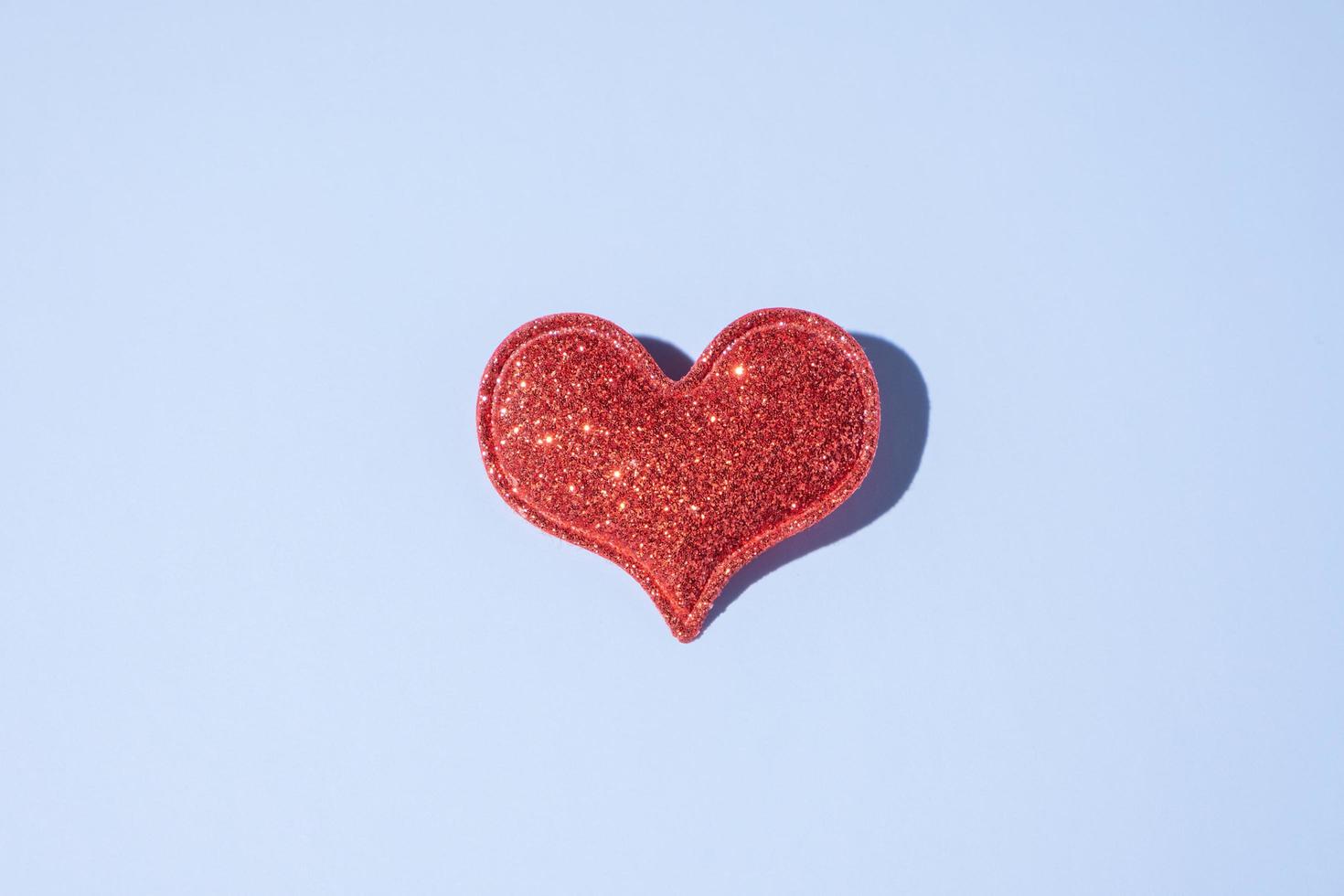 Red glitter heart shape on blue background with hard shadow. Valentines day minimalistic symbol love photo
