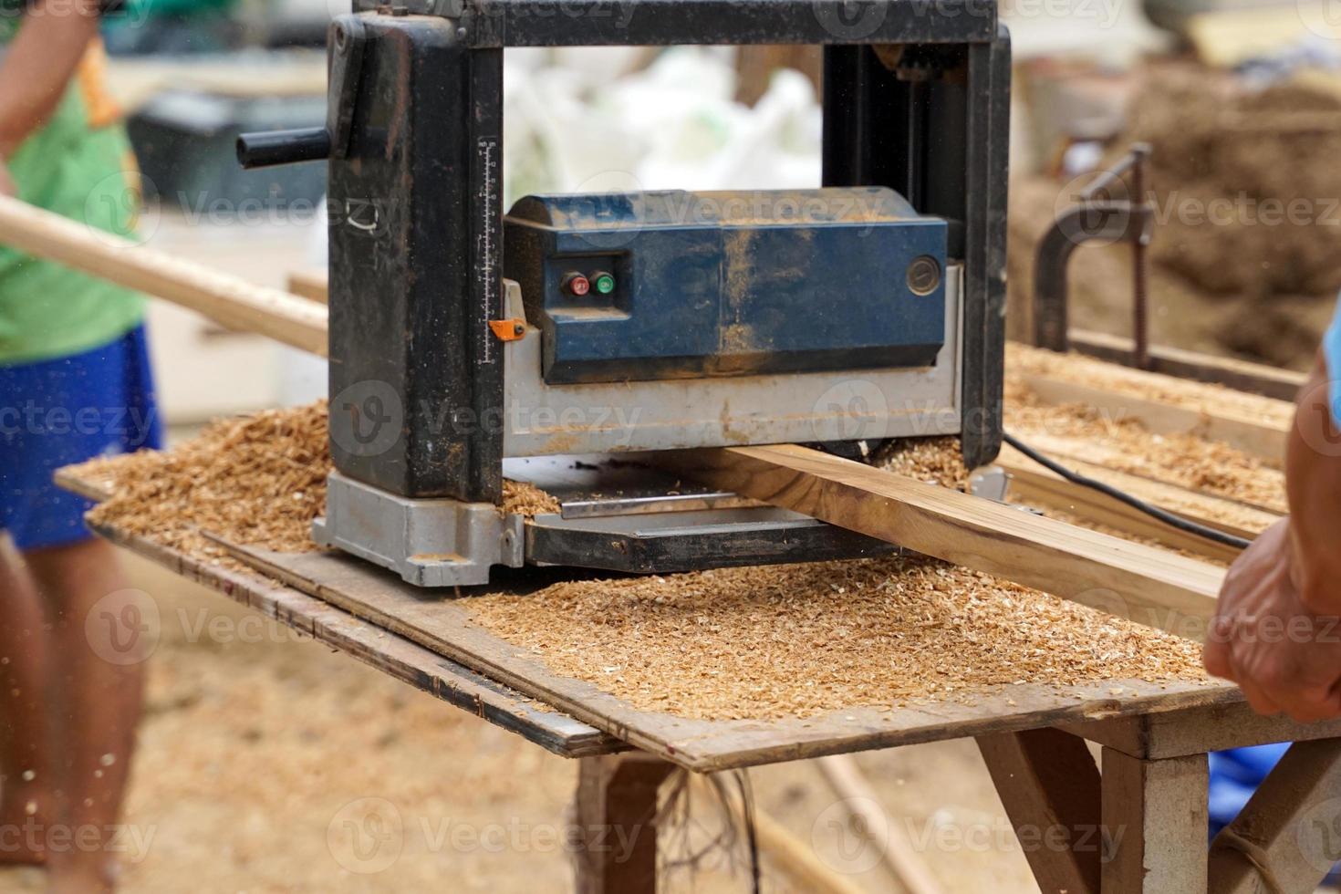 A carpenter is using a thickness planer to roll a sheet of wood to have a consistent thickness to be suitable for woodworking. Soft and selective focus. photo