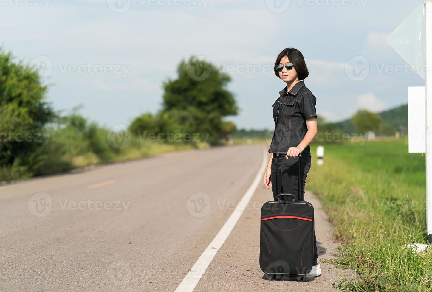 Woman with luggage hitchhiking along a road photo