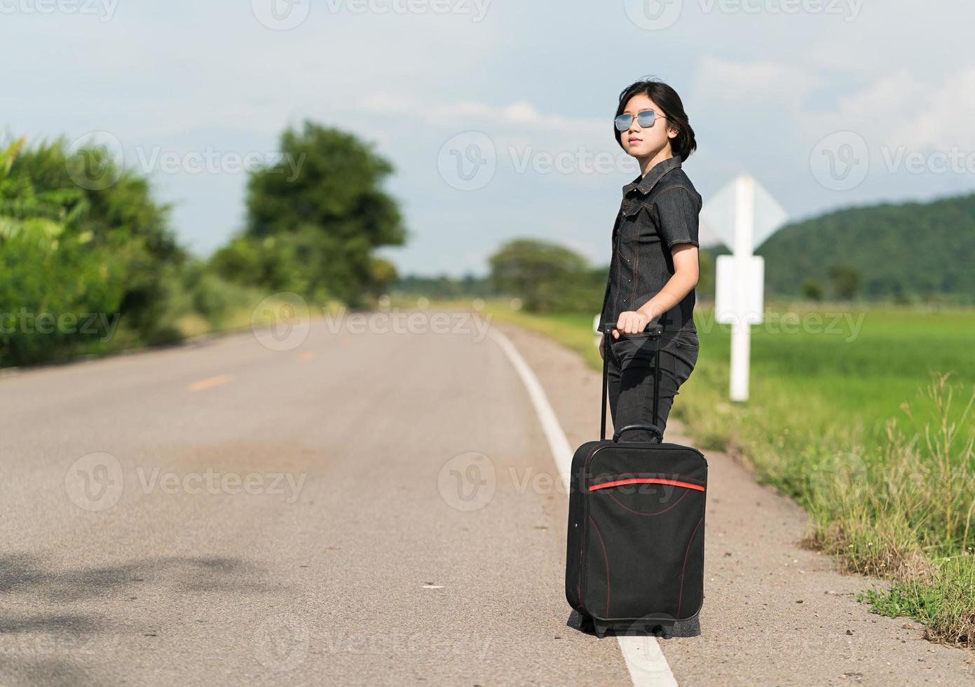 Woman with luggage hitchhiking along a road photo