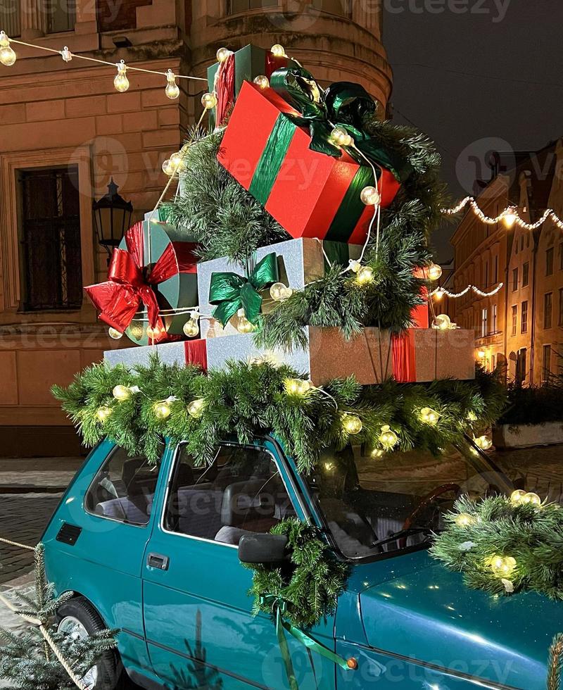 Santa's old vintage car with gift boxes on top. Closeup branches of coniferous tree decorated shiny light garland. Perfect festive content for stories background, vertical banner. photo