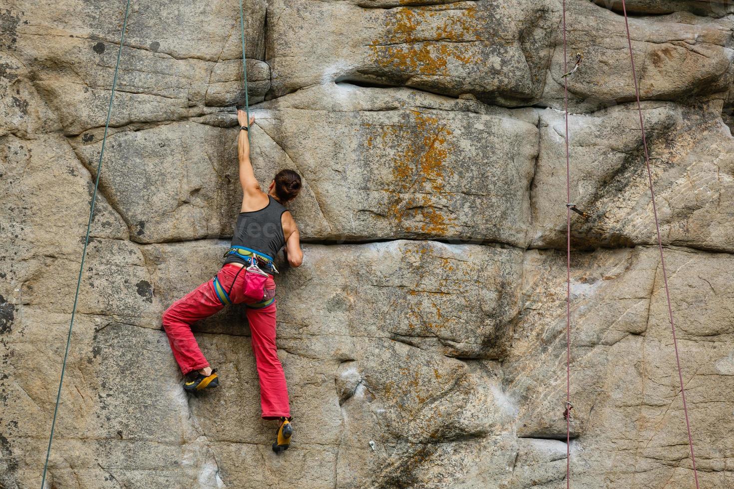 A young woman with a rope engaged in the sports of rock climbing on the rock. photo