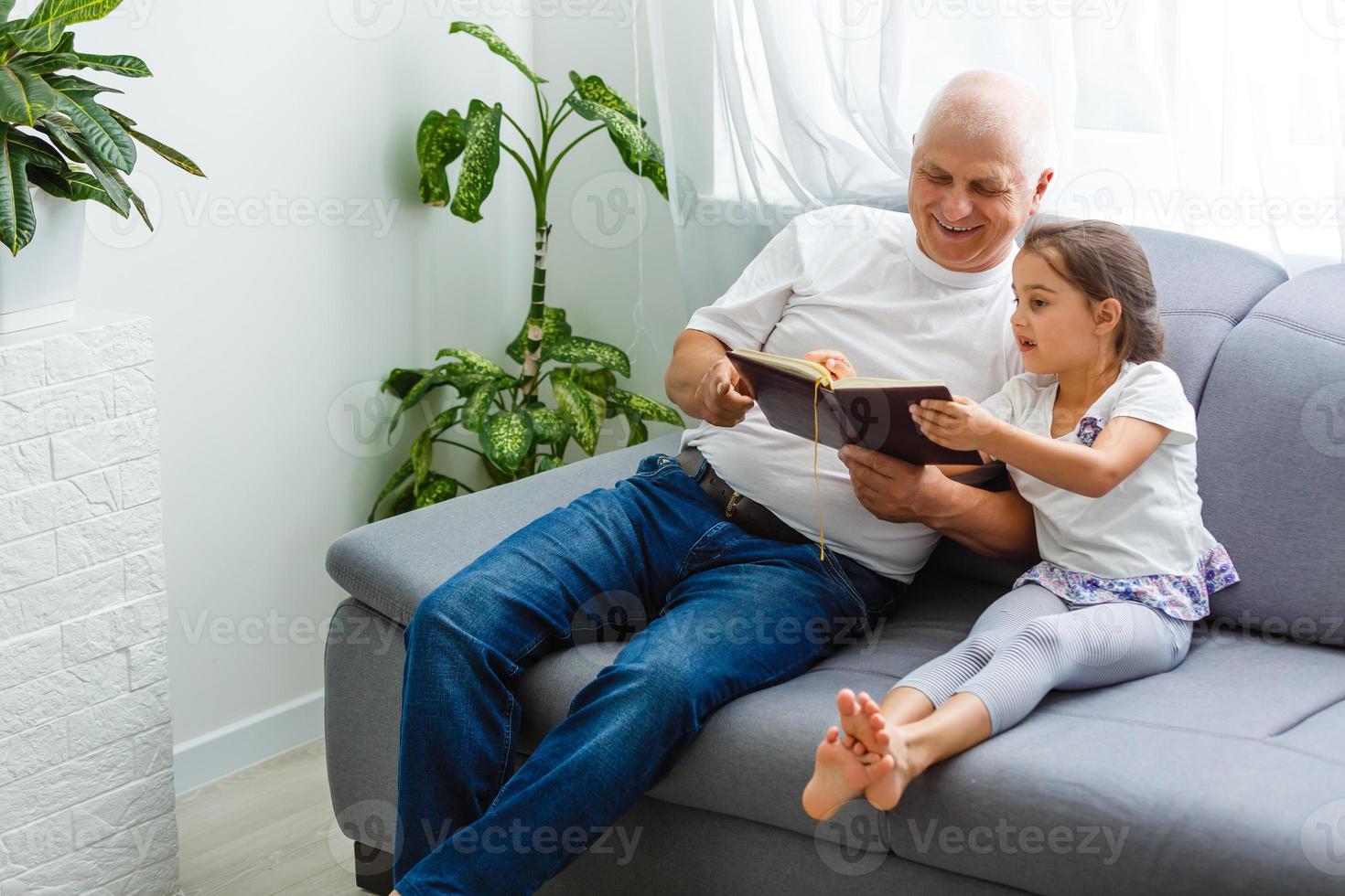 niña feliz con el abuelo leyendo un libro de cuentos en casa foto