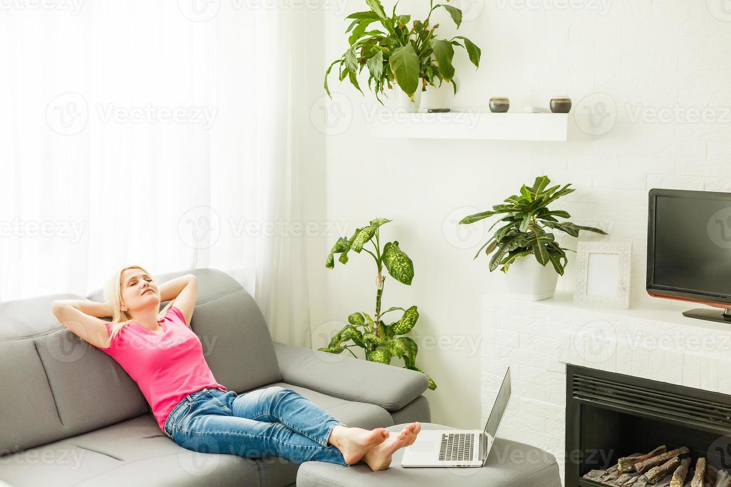 Happy young woman lying on couch and relaxing at home, casual style indoor shoot. Portrait of a girl relaxing on a sofa after work at home sitting on a sofa in the living room at home photo