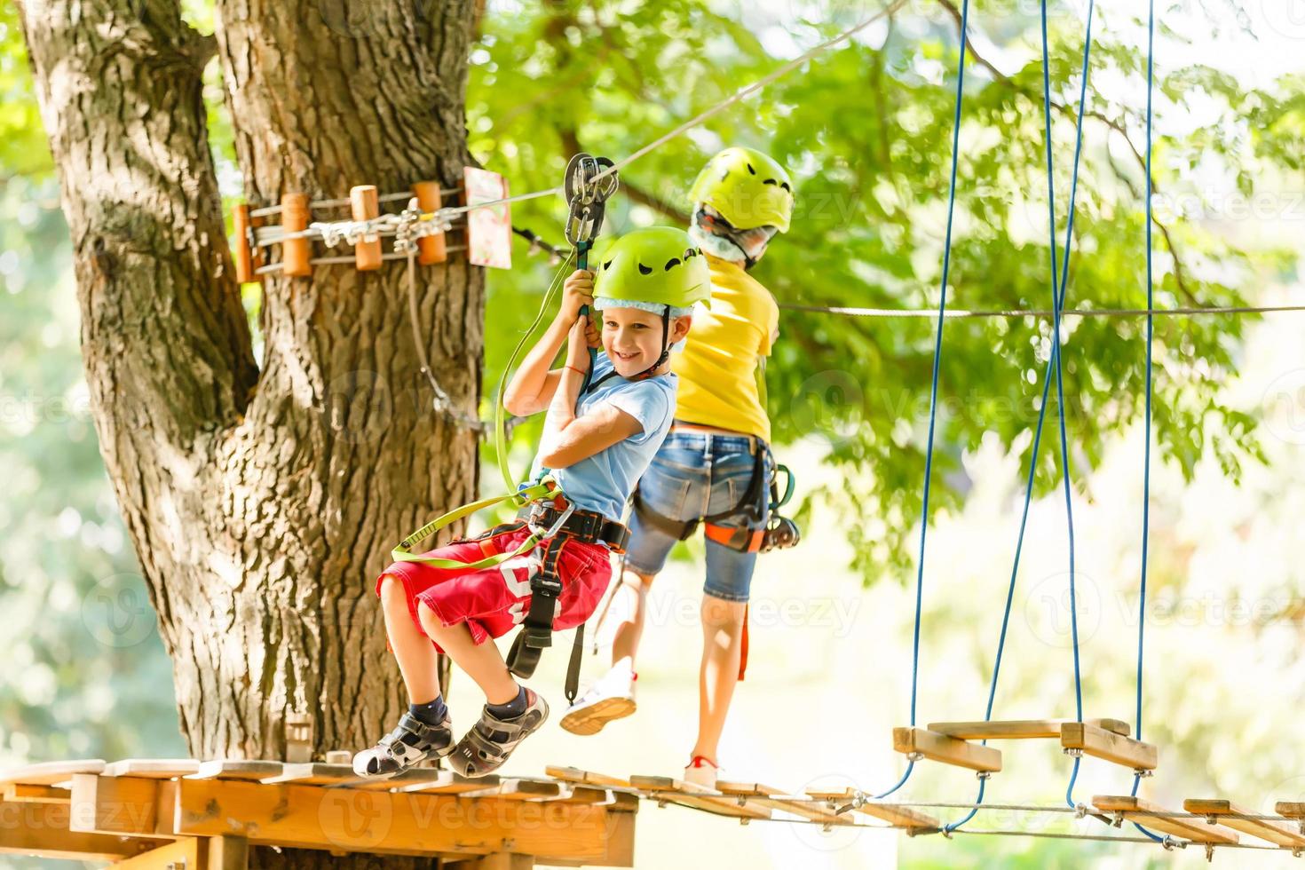 parque de cuerdas de escalada de aventura - niños en el parque de cuerdas del curso en casco de montaña y equipo de seguridad foto