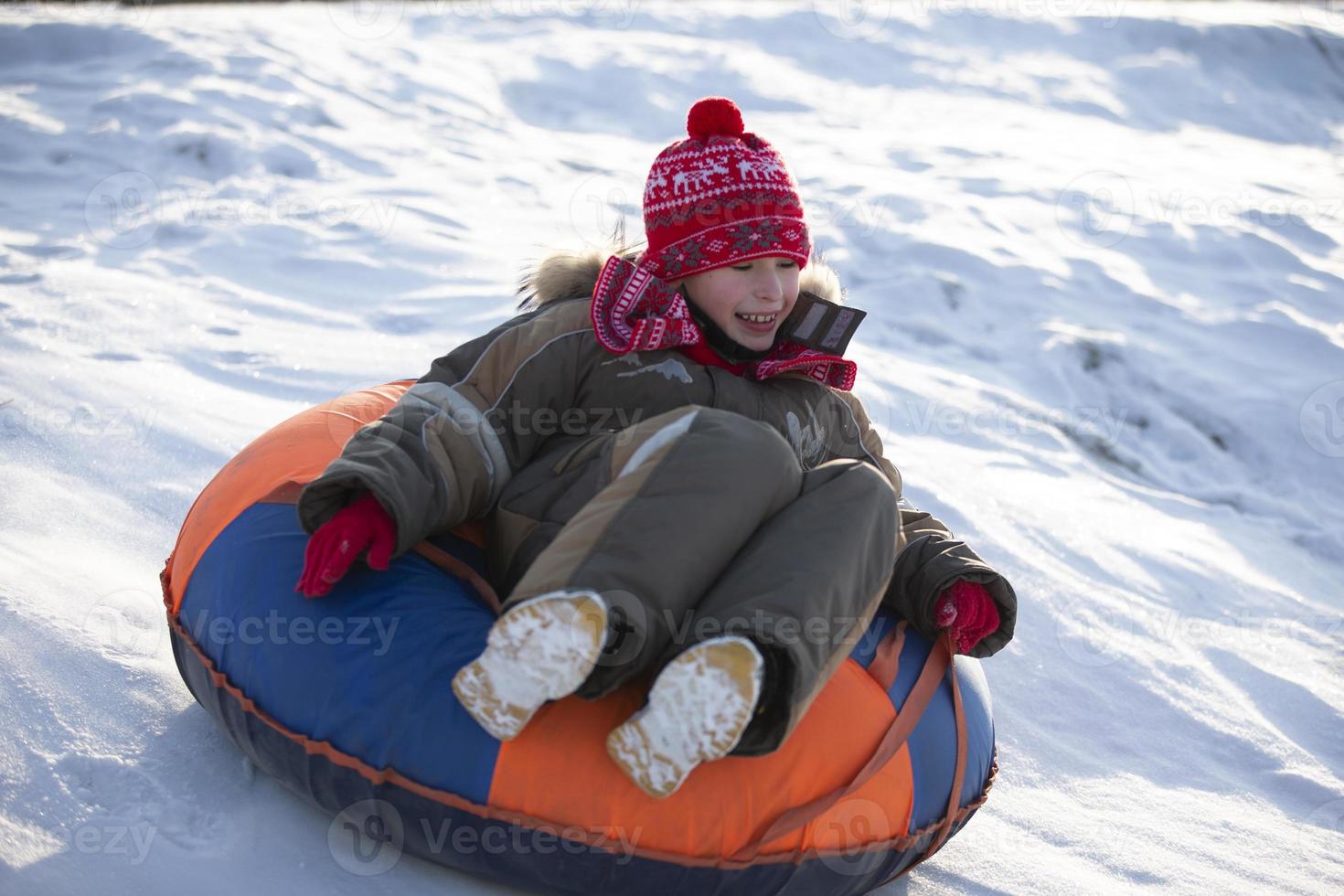 A happy boy up in the air on a tube sledding in the snow.. A boy slides down a hill in winter. photo