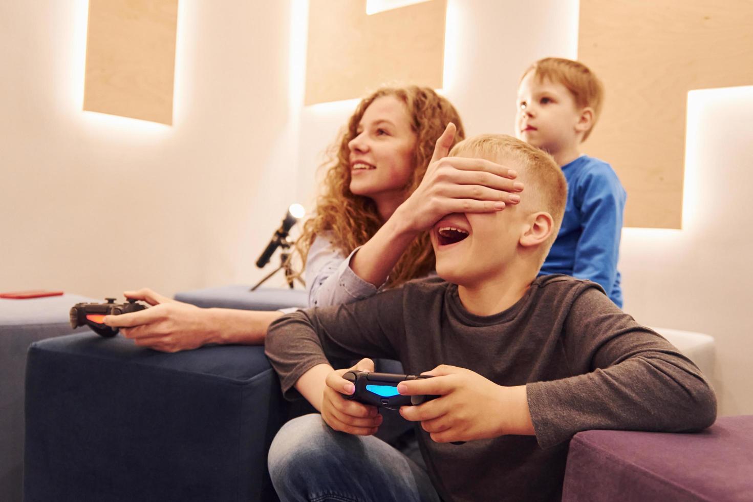 Cheerful kids sitting indoors and playing video games together photo