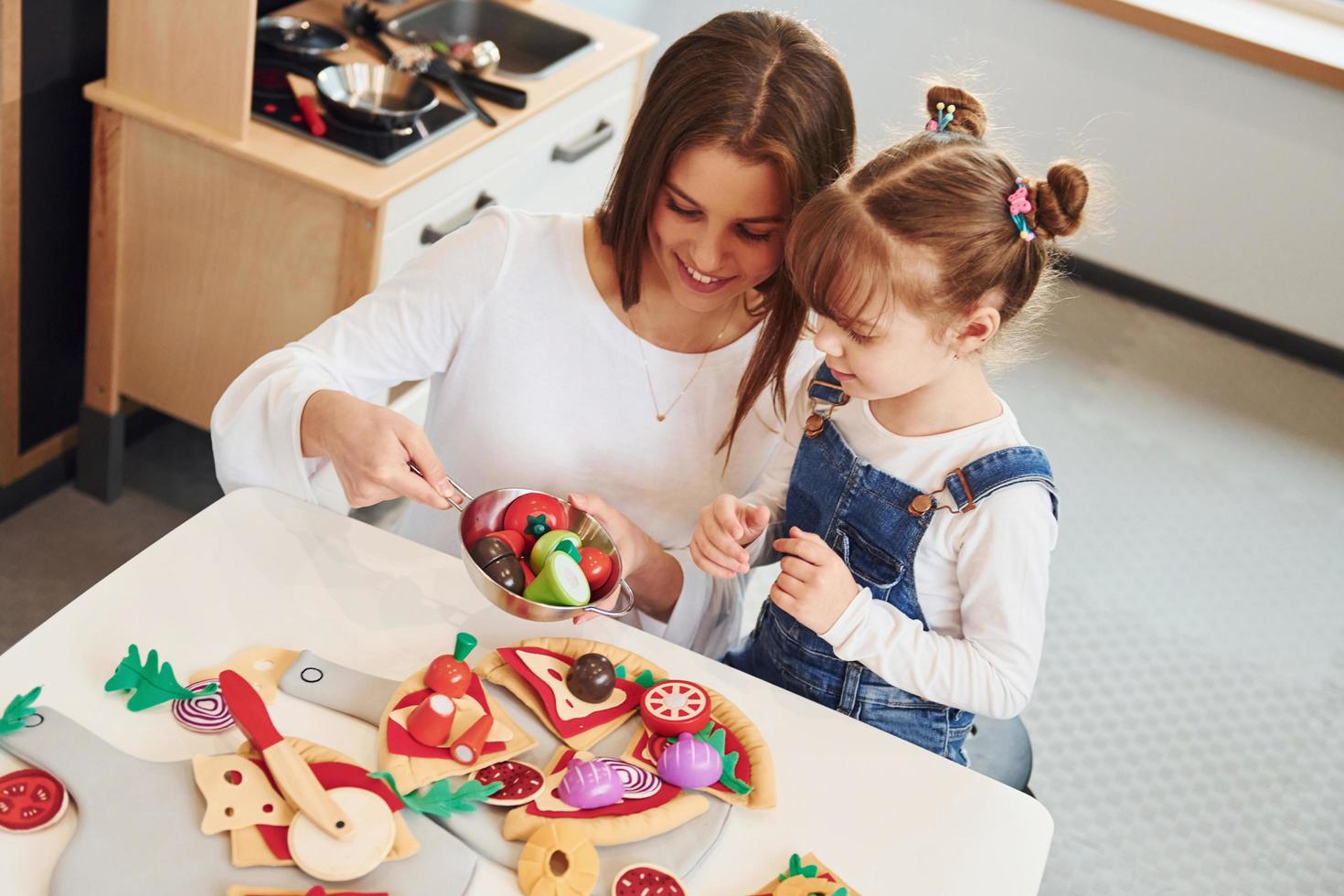 mujer joven con niña jugando con juguetes juntos en la cocina foto