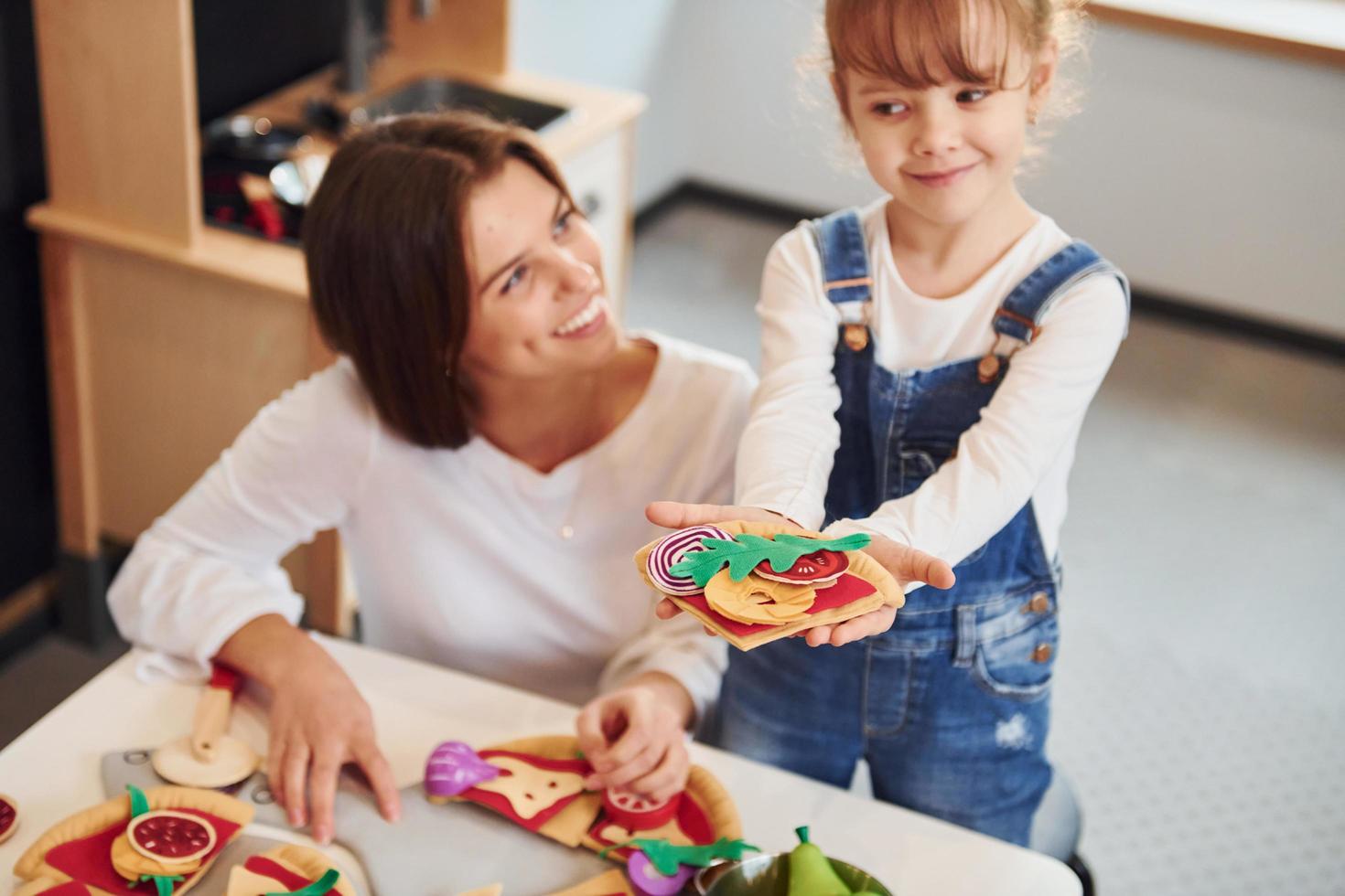 mujer joven con niña jugando con juguetes juntos en la cocina foto