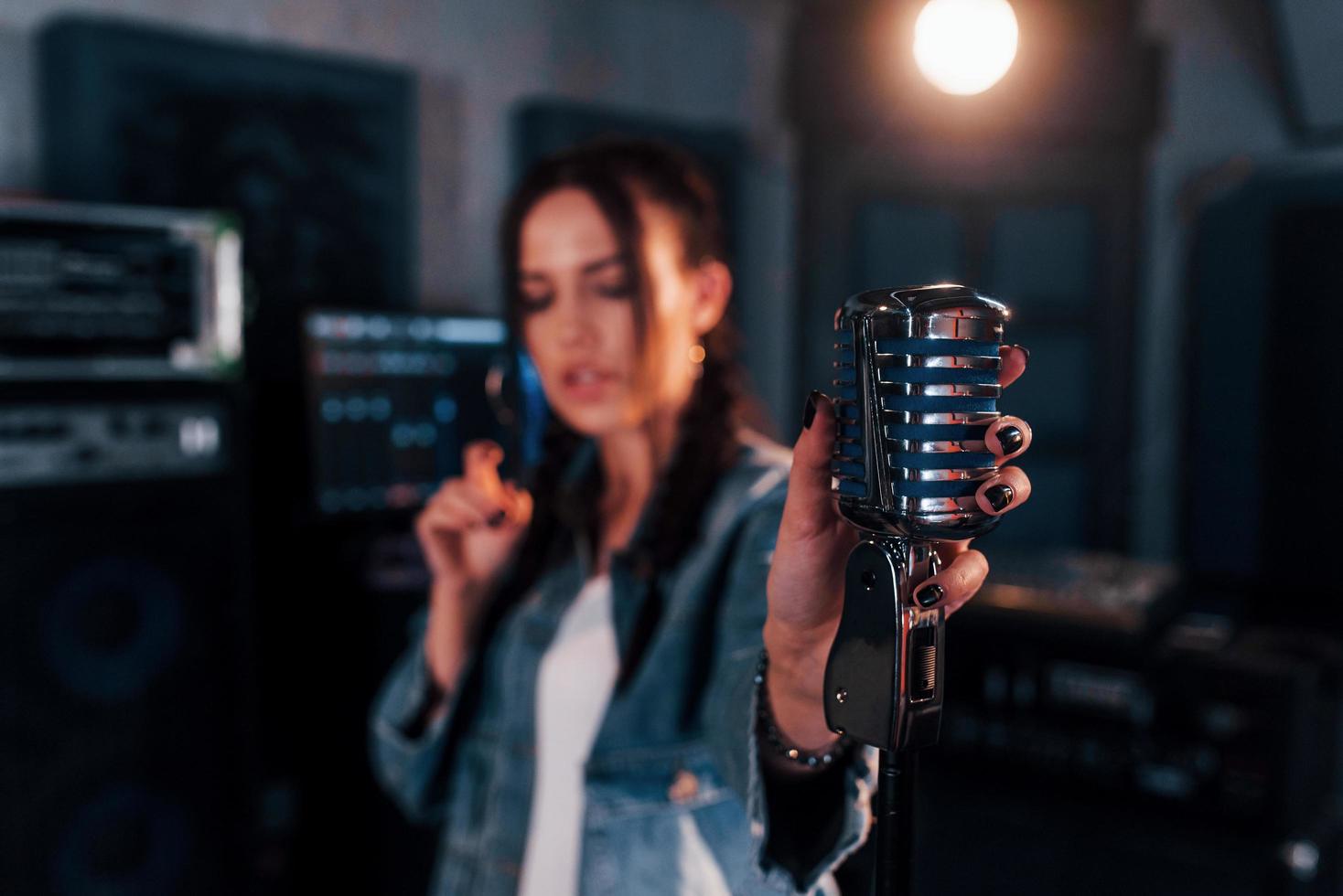 Close up view of microphone. Young beautiful female performer rehearsing in a recording studio photo