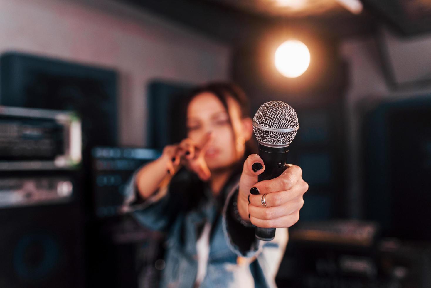 vista de cerca del micrófono. joven y bella intérprete femenina ensayando en un estudio de grabación foto