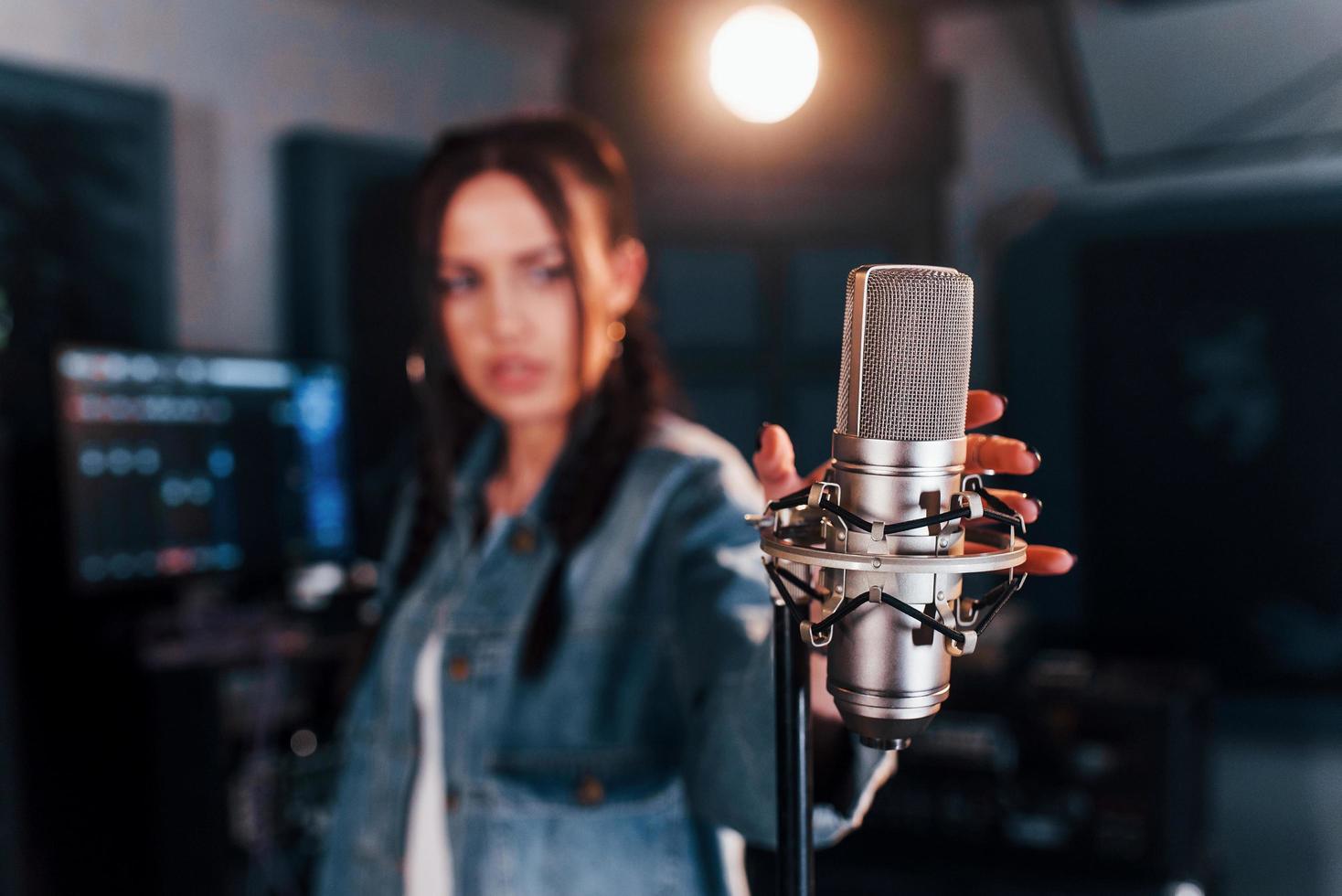 Close up view of microphone. Young beautiful female performer rehearsing in a recording studio photo