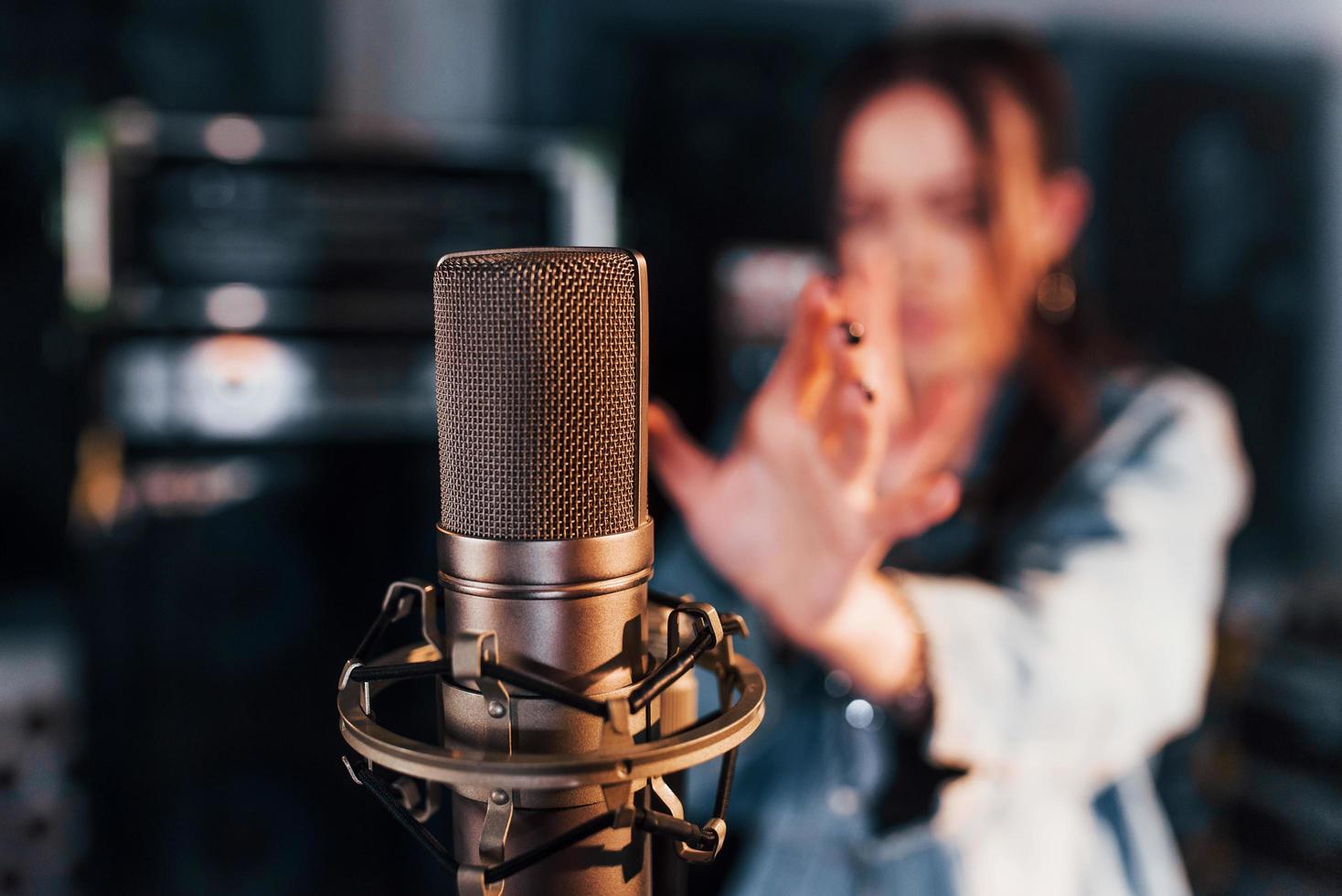 Close up view of microphone. Young beautiful female performer rehearsing in a recording studio photo