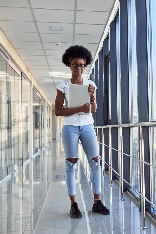 una joven pasajera afroamericana con ropa informal está en el aeropuerto sosteniendo una laptop foto
