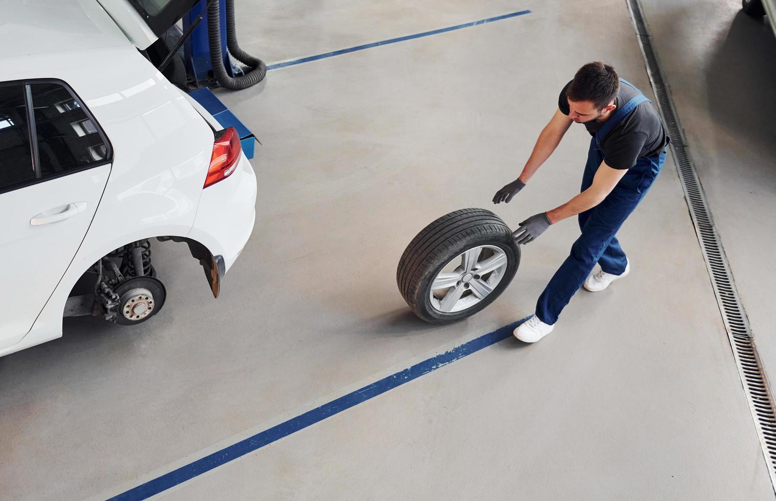 Top view. Man in work uniform walking with car wheel indoors. Conception of automobile service photo