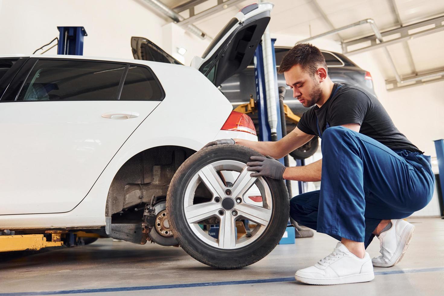 Man in work uniform changing car wheel indoors. Conception of automobile service photo