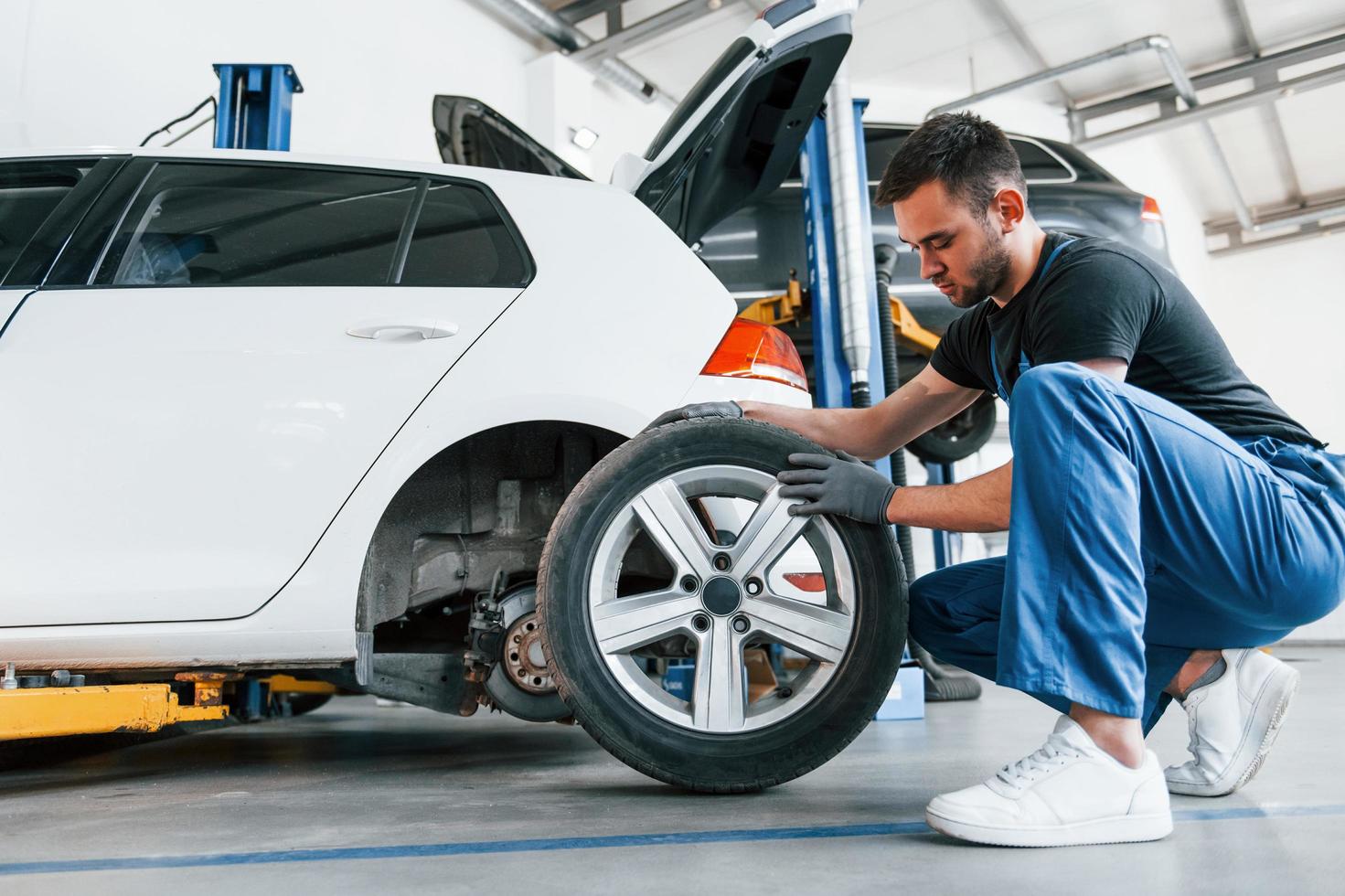 hombre con uniforme de trabajo cambiando la rueda del coche en el interior. concepción del servicio del automóvil foto