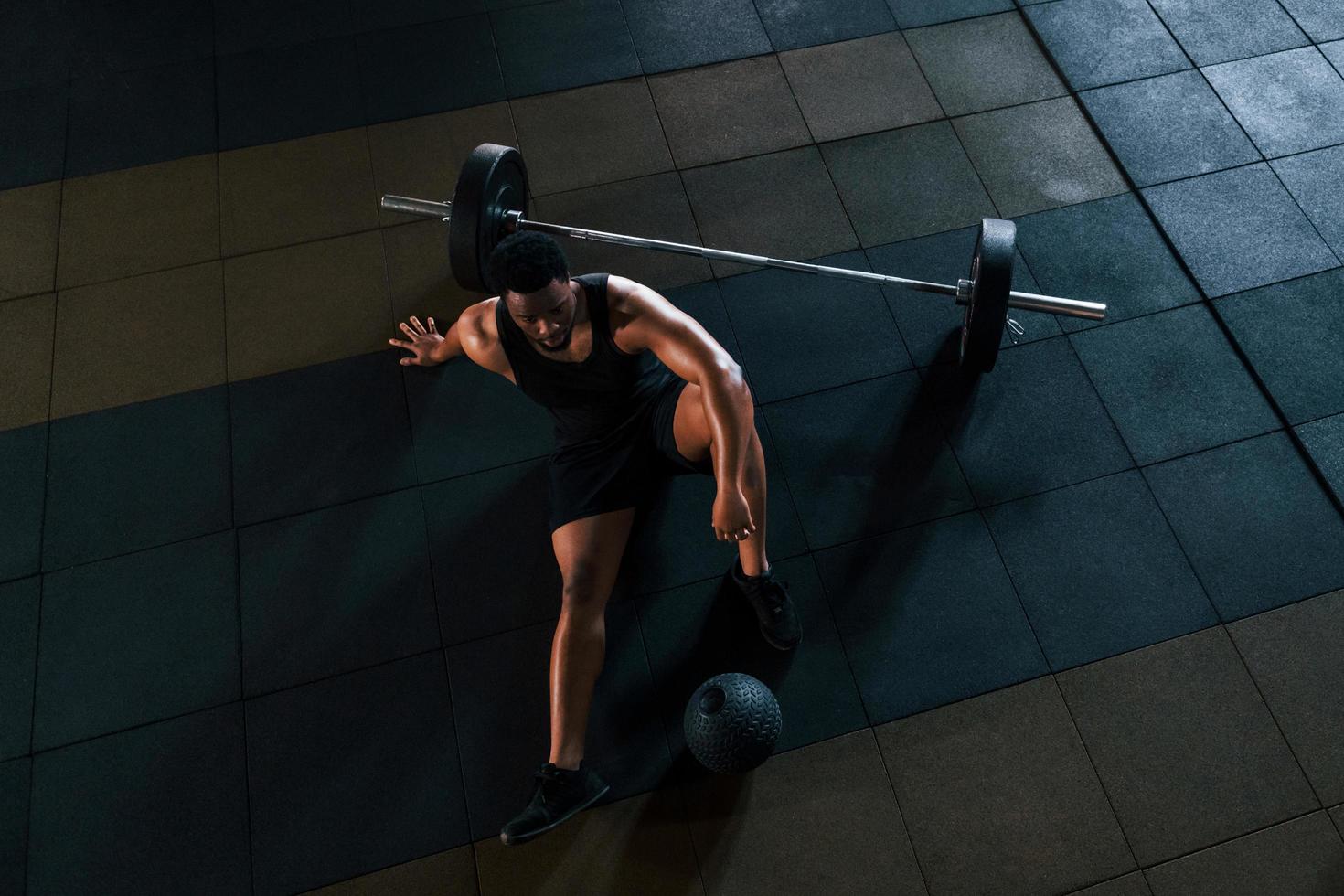 Sitting on the floor. Strong african american man in sportive clothes have workout day in the gym photo