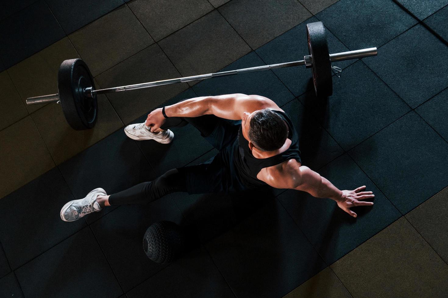 vista superior de un hombre fuerte con ropa deportiva que se sienta en el suelo y toma un descanso en el gimnasio foto