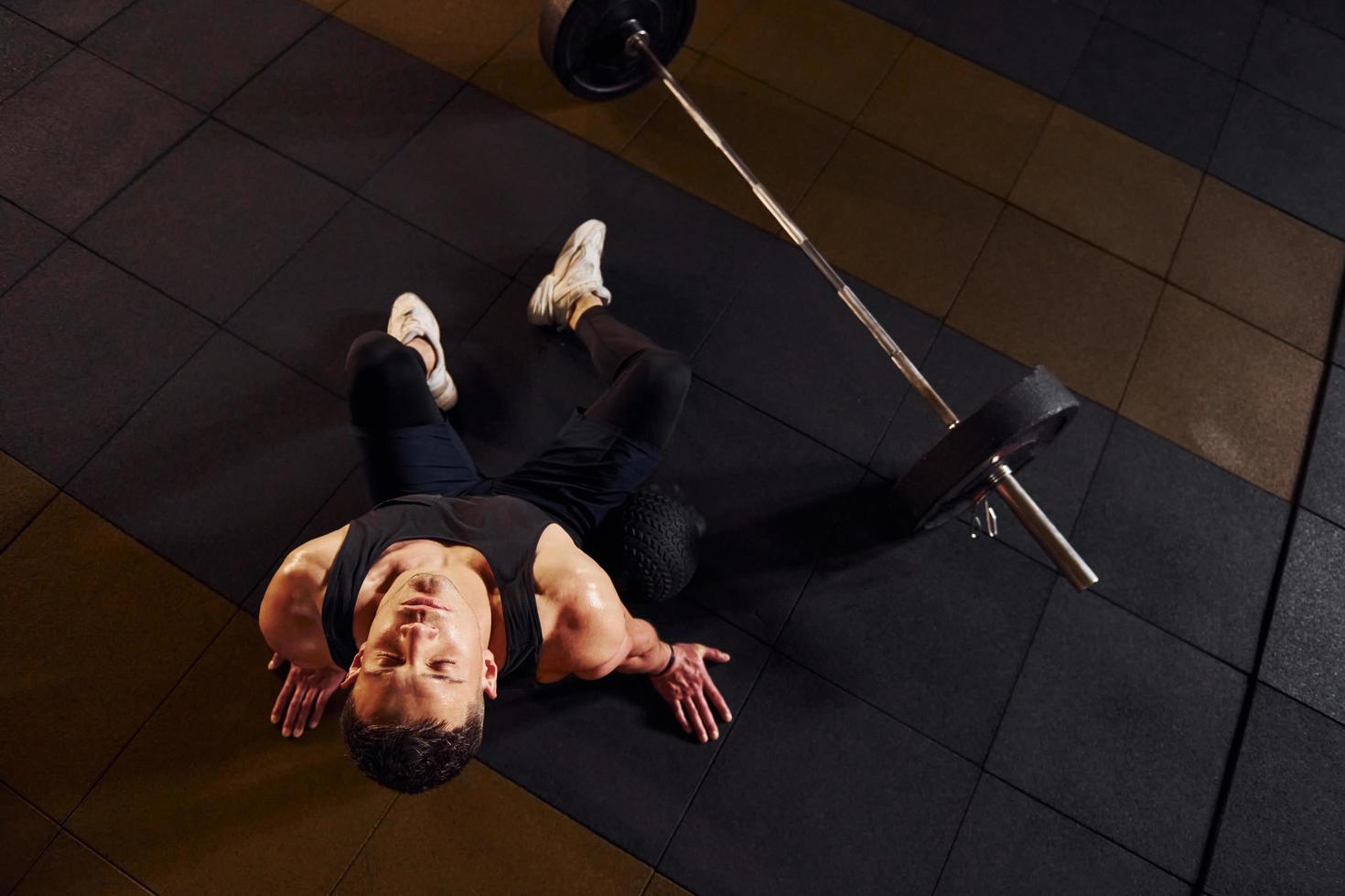 vista superior de un hombre fuerte con ropa deportiva que se sienta en el suelo y toma un descanso en el gimnasio foto