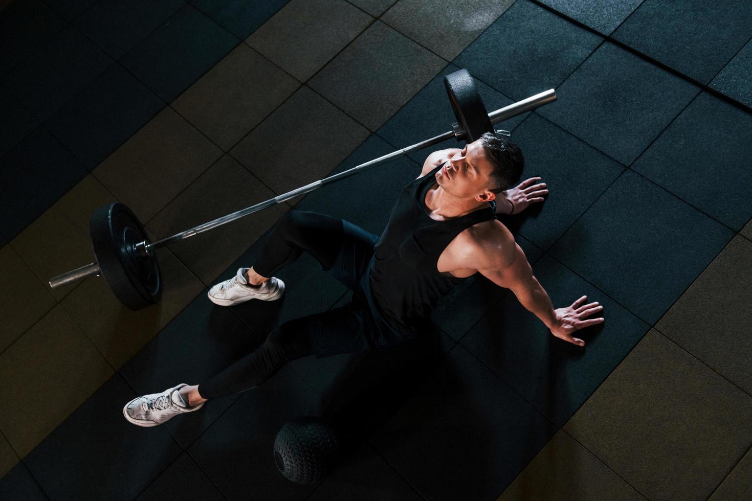 Top view of strong man in sportive clothes that sitting on the floor and takes a break in the gym photo