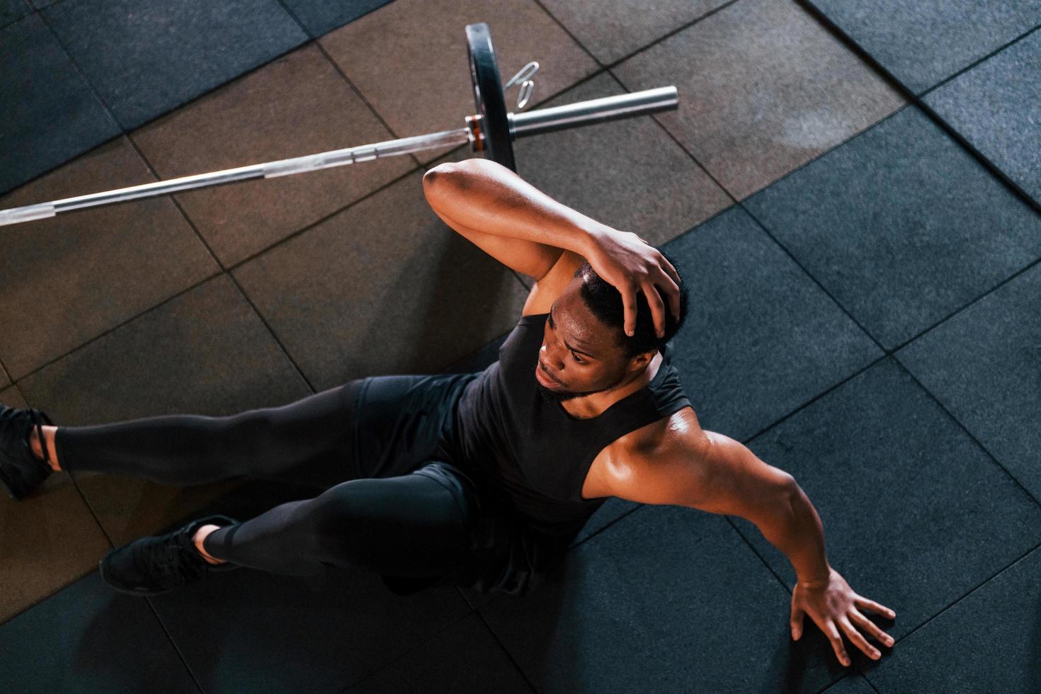 Sitting on the floor. Strong african american man in sportive clothes have workout day in the gym photo