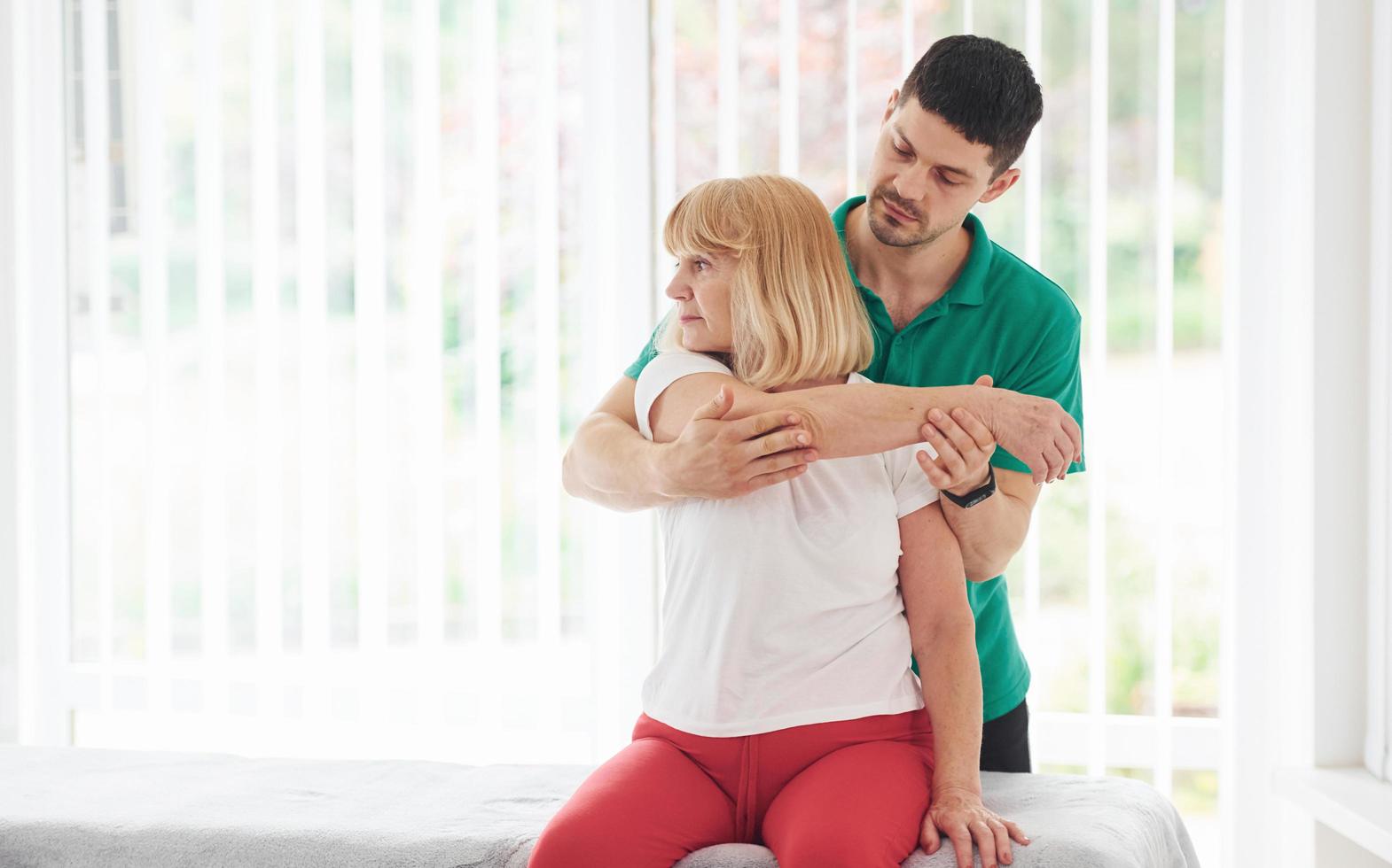 la mujer mayor tiene una visita en la clínica y tiene rehabilitación. instructor masculino ayudándola foto