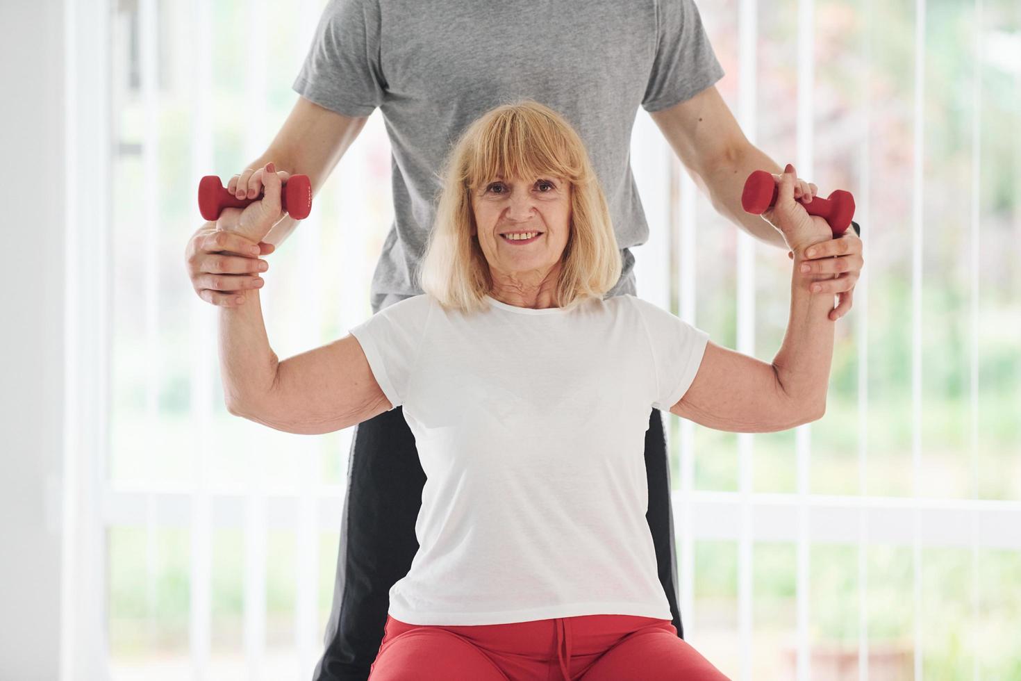 Older woman have a visit in clinic and having rehabilitation. Male instructor helping her photo