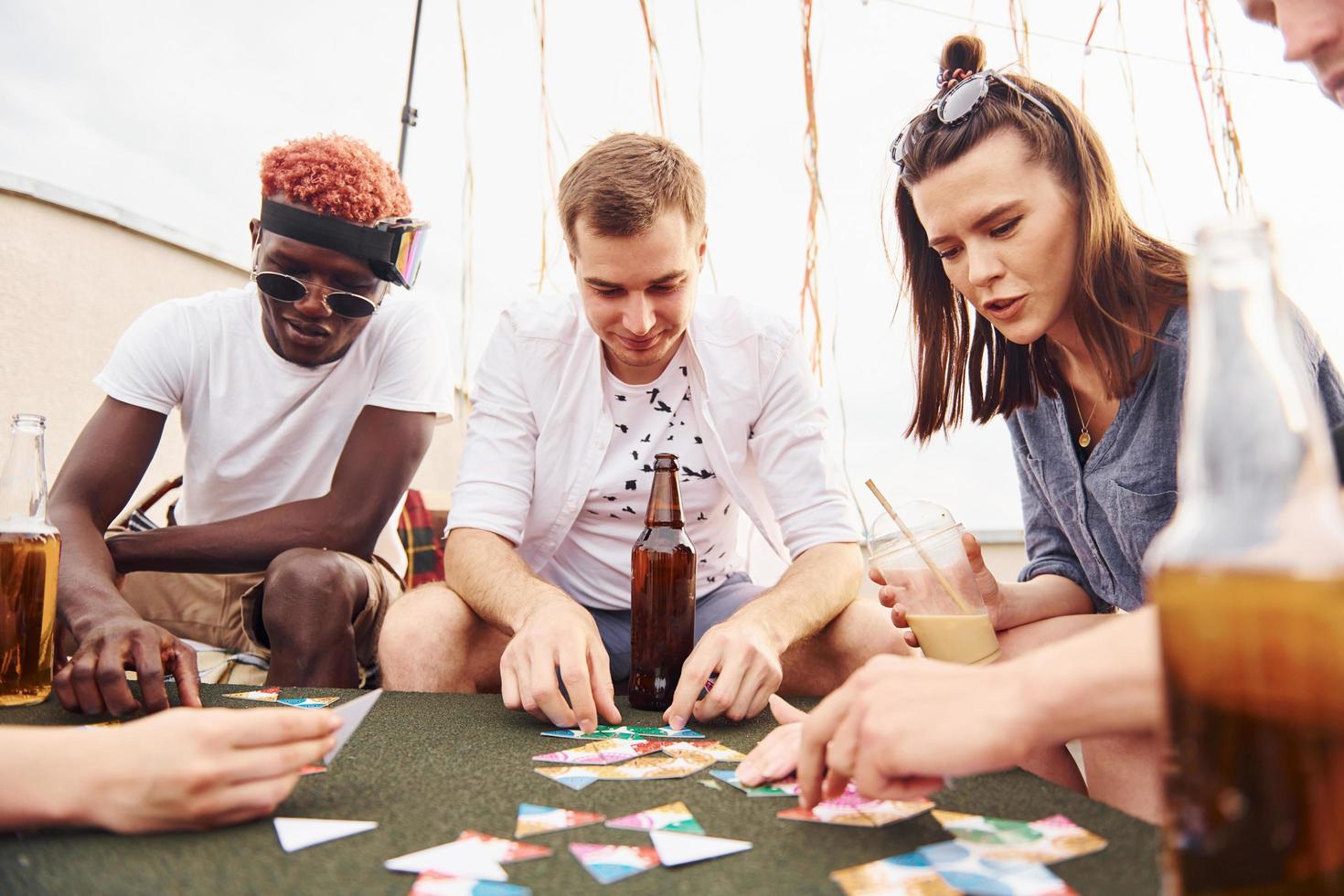 Playing card game. Group of young people in casual clothes have a party at rooftop together at daytime photo