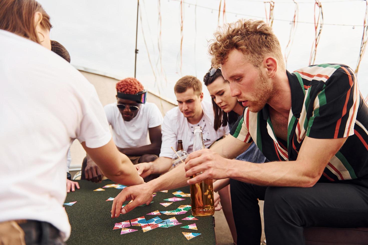 Playing card game. Group of young people in casual clothes have a party at rooftop together at daytime photo