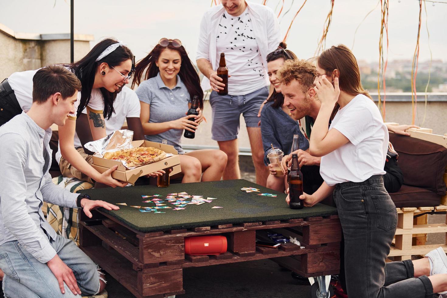 With delicious pizza. Group of young people in casual clothes have a party at rooftop together at daytime photo