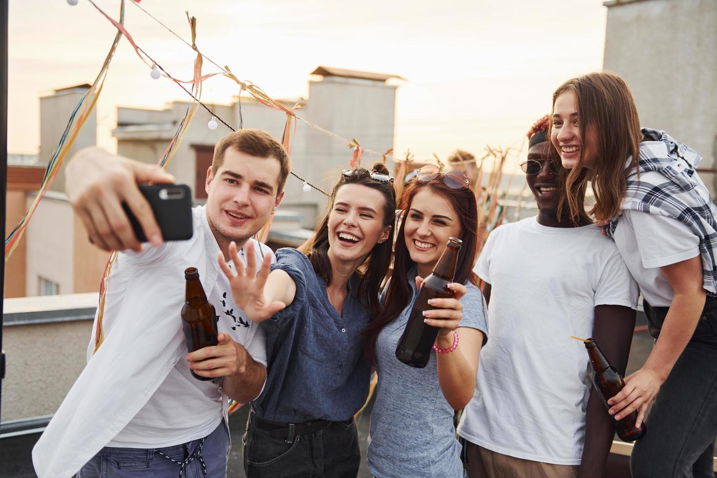 Group of young people in casual clothes have a party at rooftop together at daytime and doing selfie by phone photo