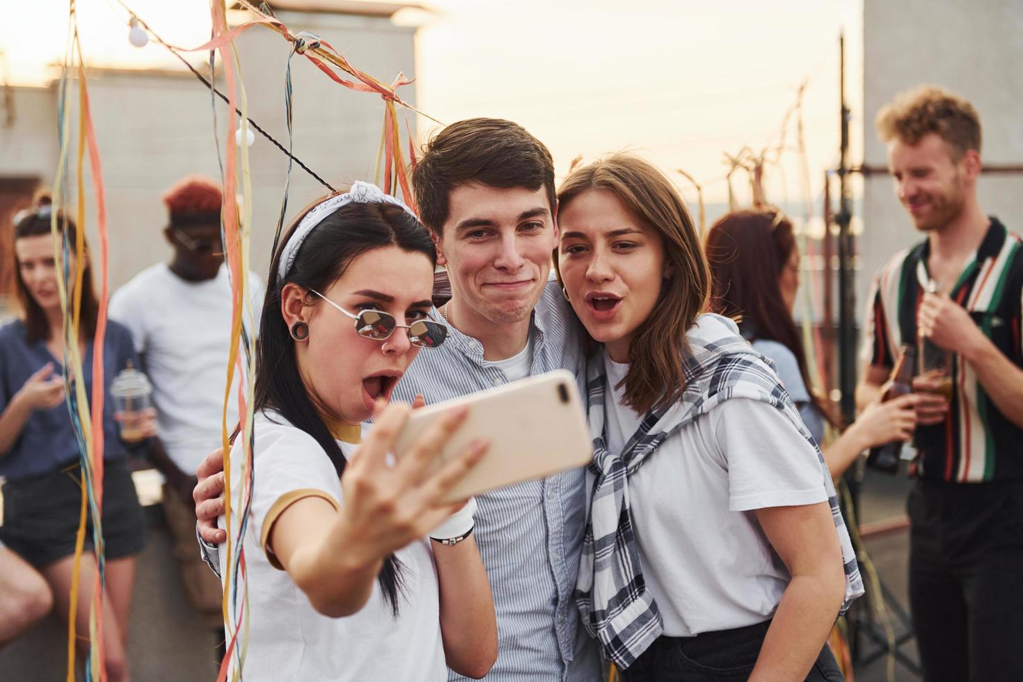 tomando autofoto. un grupo de jóvenes con ropa informal tienen una fiesta en la azotea juntos durante el día foto