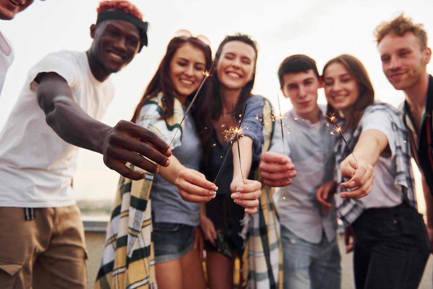 con bengalas en las manos. un grupo de jóvenes con ropa informal tienen una fiesta en la azotea juntos durante el día foto