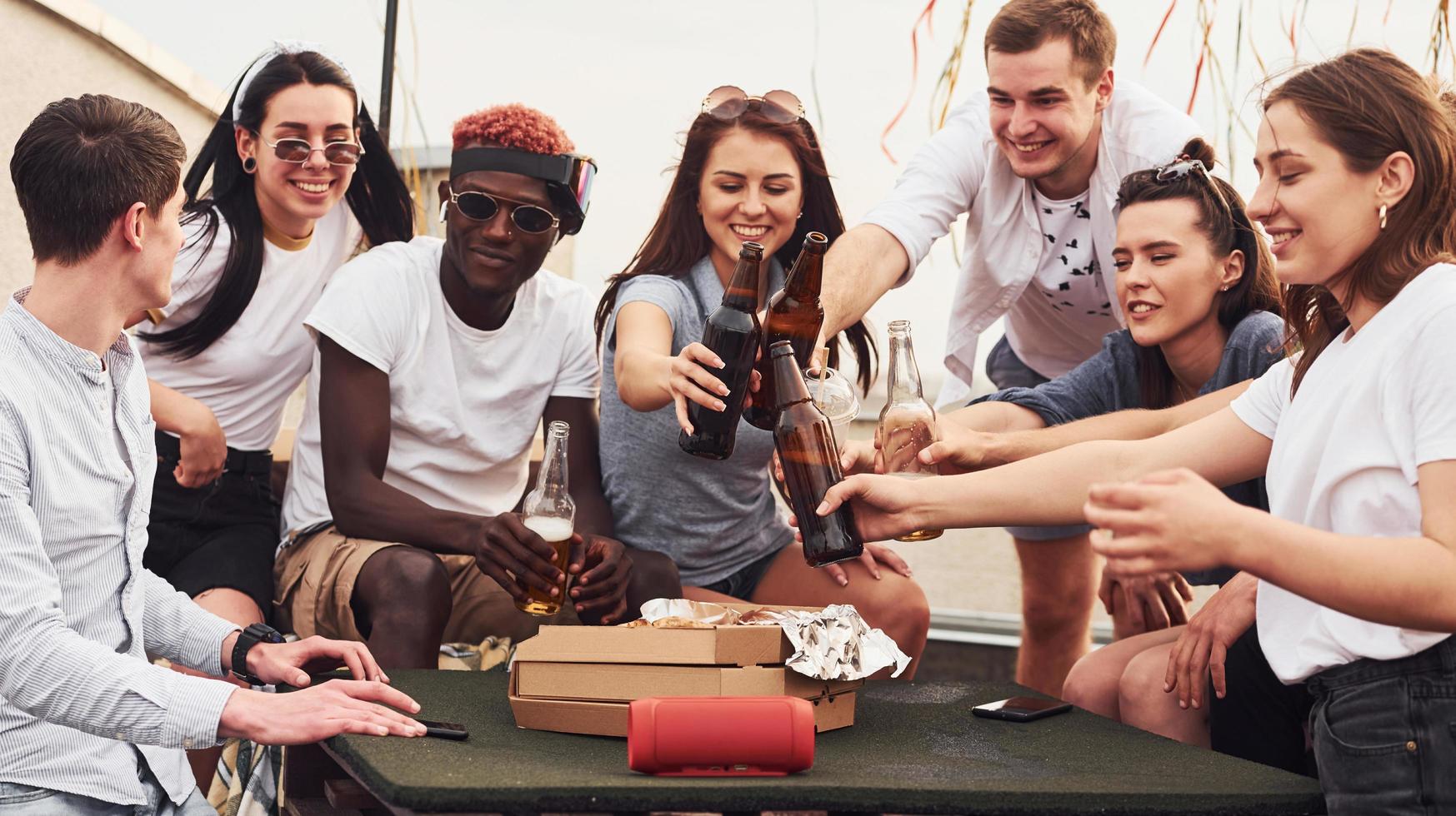 deliciosa pizza un grupo de jóvenes con ropa informal tienen una fiesta en la azotea juntos durante el día foto