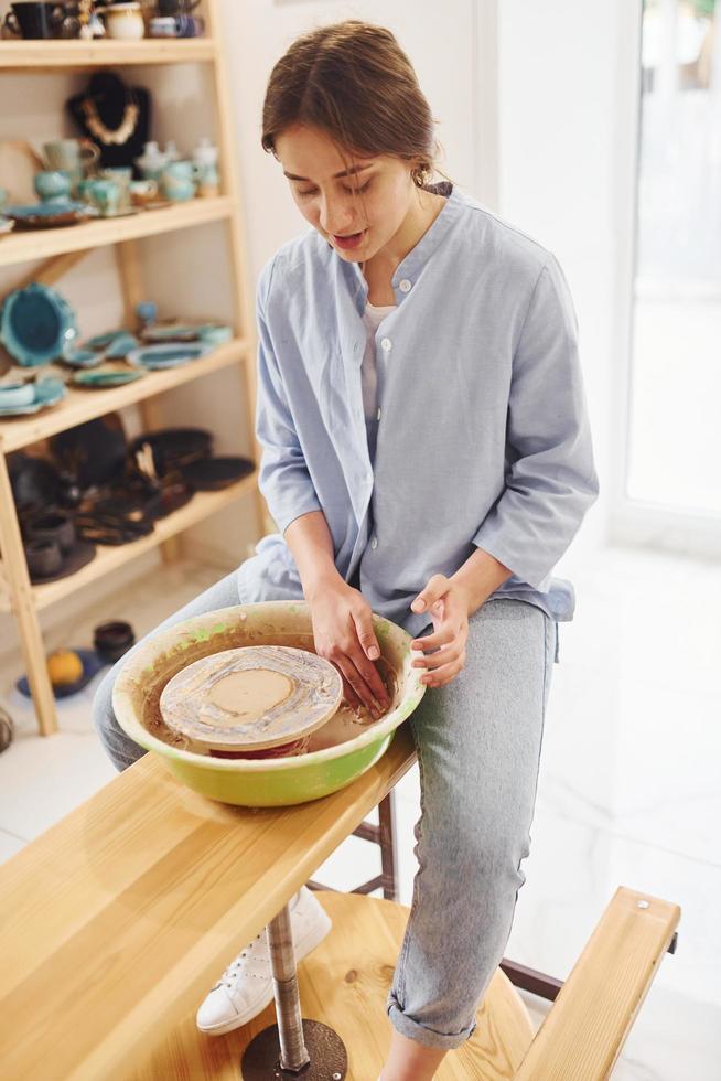 Young female ceramist working by using pottery wheel indoors and making handmade clay product photo