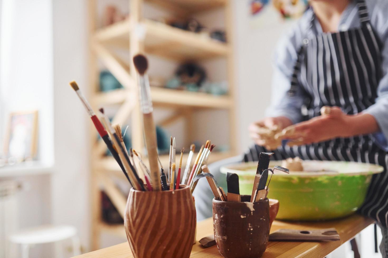 Young female ceramist working by using pottery wheel indoors and making handmade clay product photo