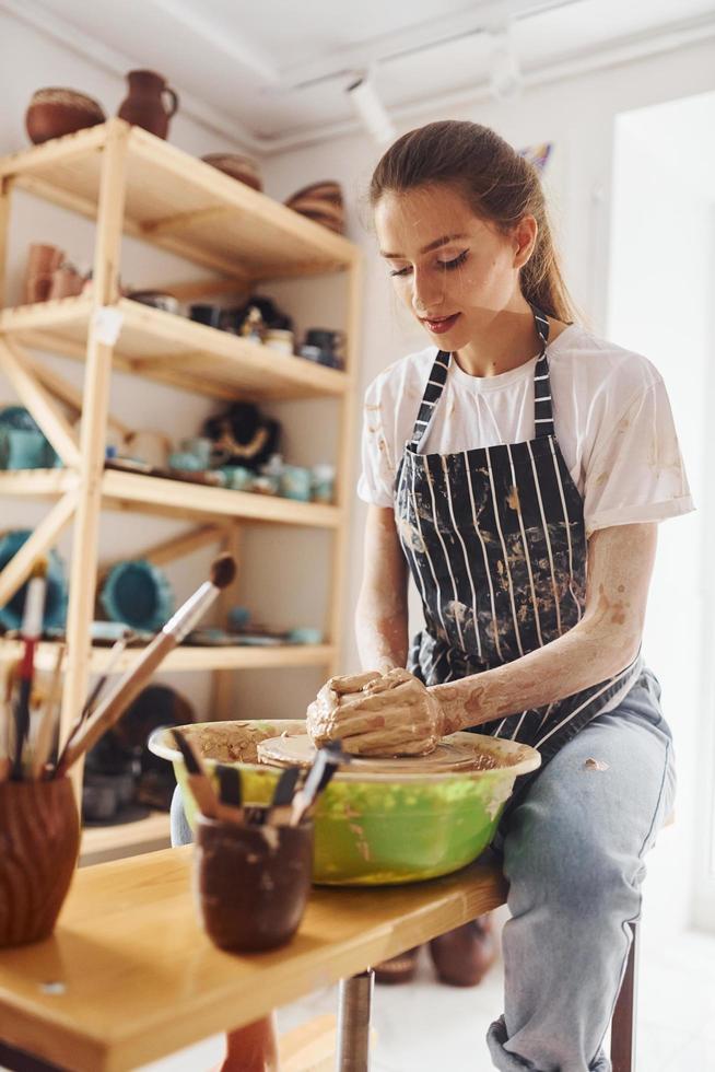Young female ceramist working by using pottery wheel indoors and making handmade clay product photo