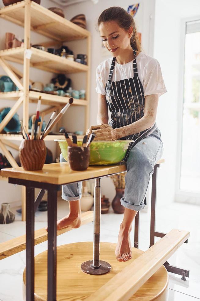 Young female ceramist working by using pottery wheel indoors and making handmade clay product photo