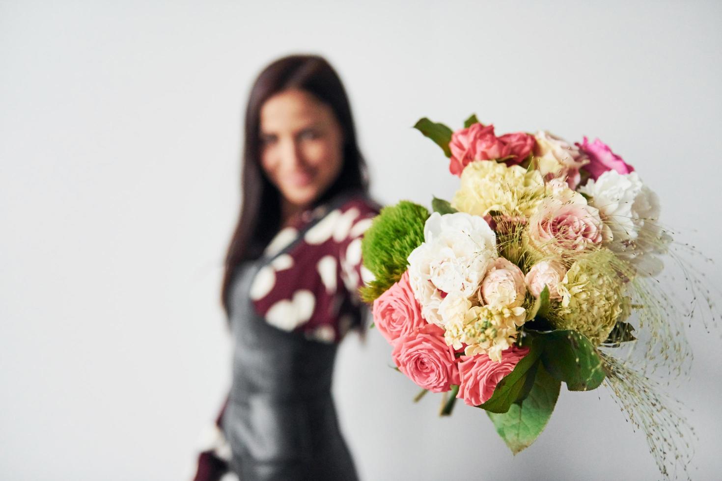 Beautiful young brunette in black skirt standing indoors against white background with bouquet in hands photo