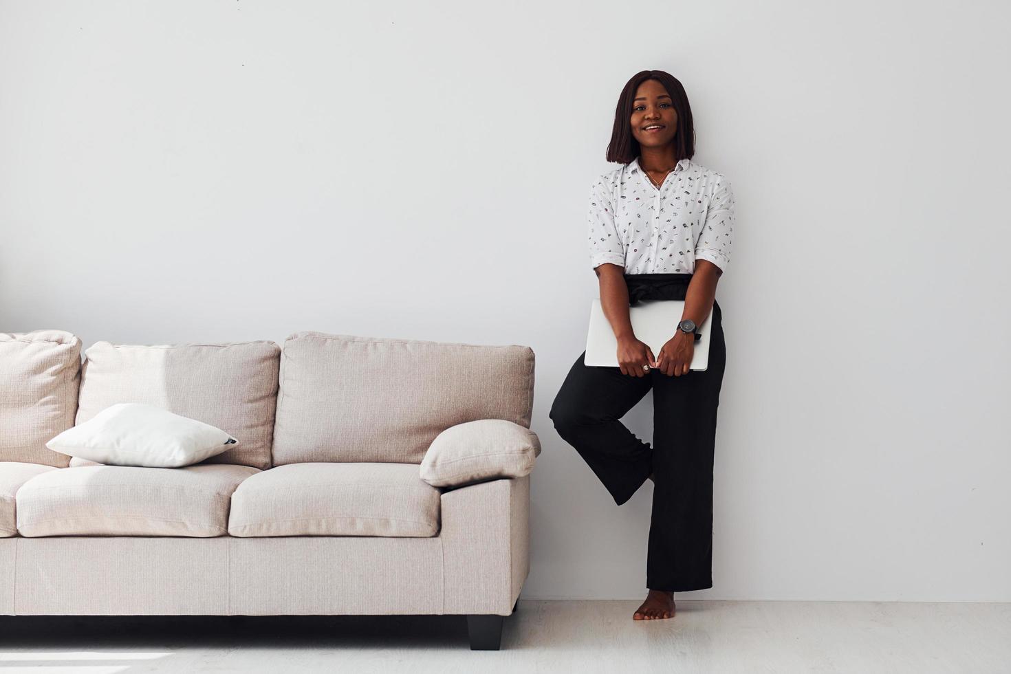 Young african american woman in formal clothes standing with laptop in hands indoors photo