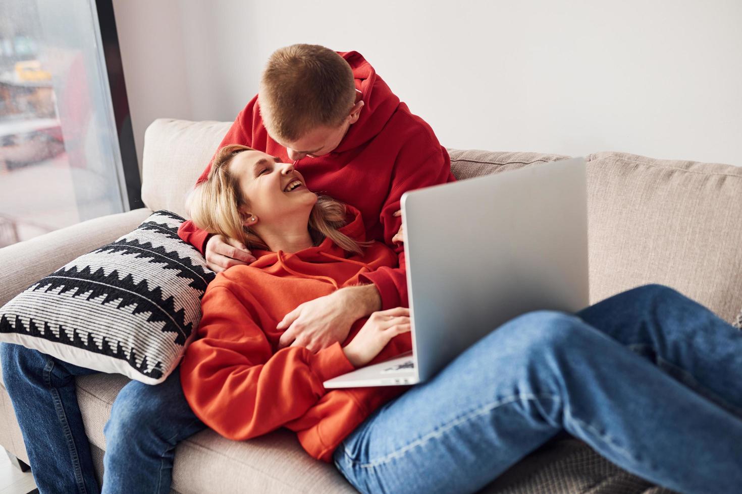 Using laptop that is on the legs. Young lovely couple together at home spending weekend and holidays together photo