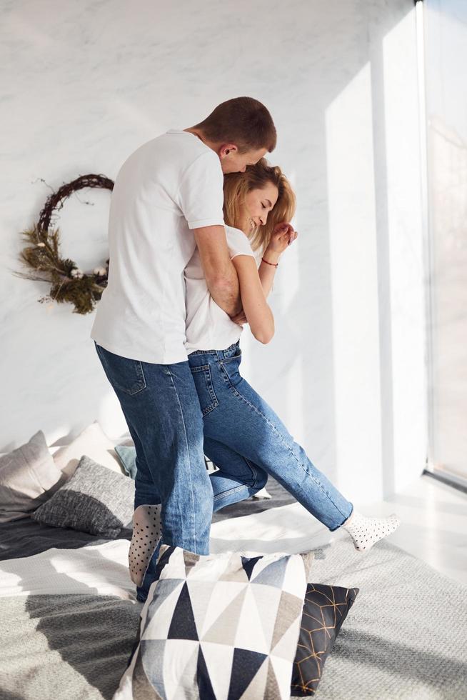 Standing and embracing on bed. Young lovely couple together at home spending weekend and holidays together photo