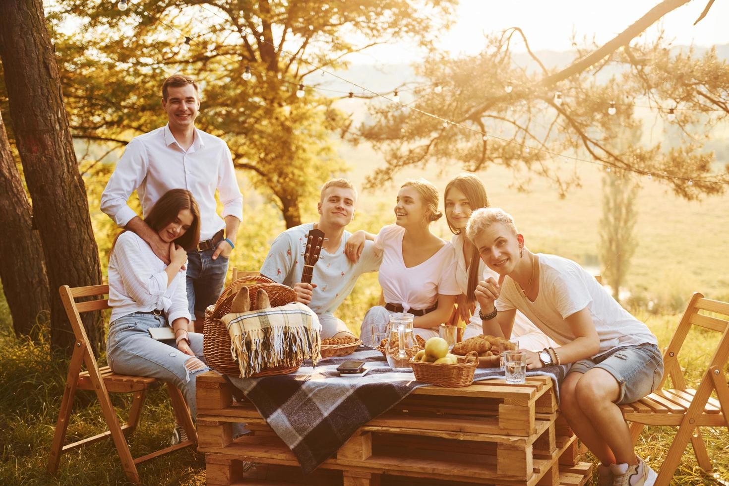 Sitting by picnic table. Group of young people have vacation outdoors in the forest. Conception of weekend and friendship photo