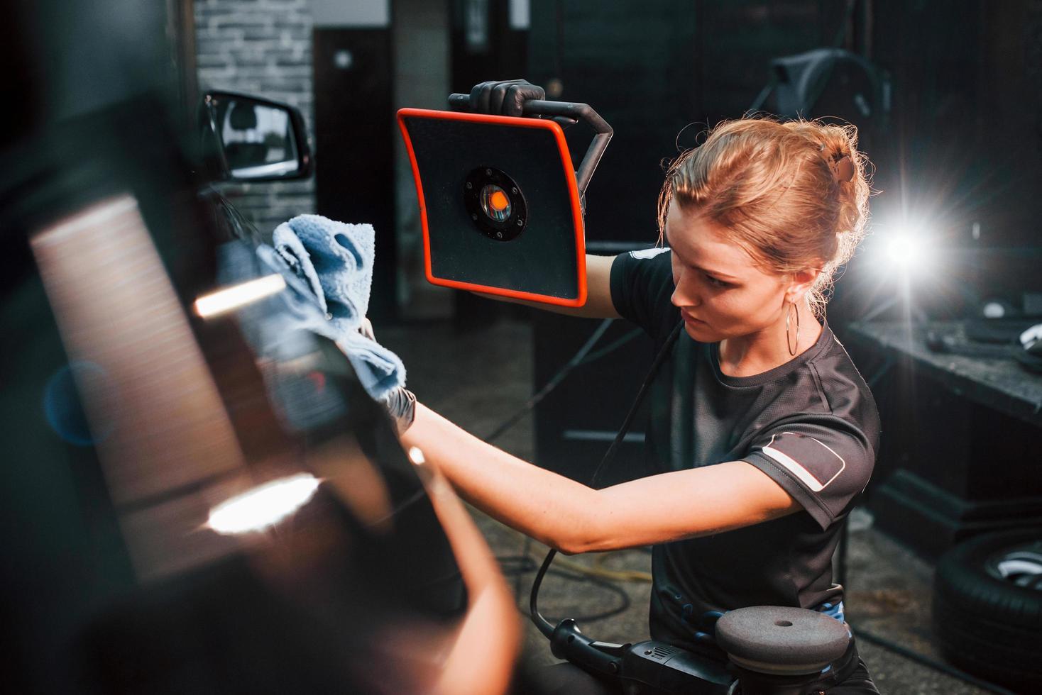 Final polishing. Modern black automobile get cleaned by woman inside of car wash station photo